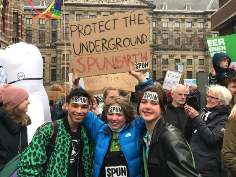 three young people smile holding a sign that reads 'protect the underground'