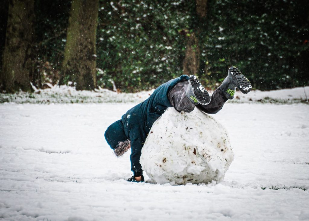 Kid jumps on giant snowball in a snowy field