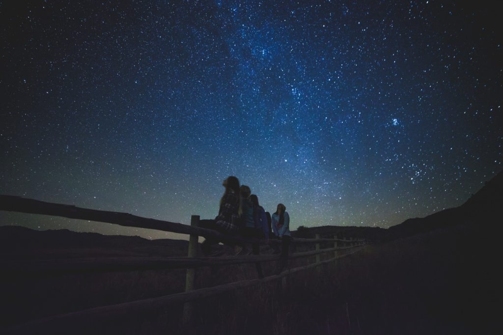 Group of people sit on a fence at night and stargaze