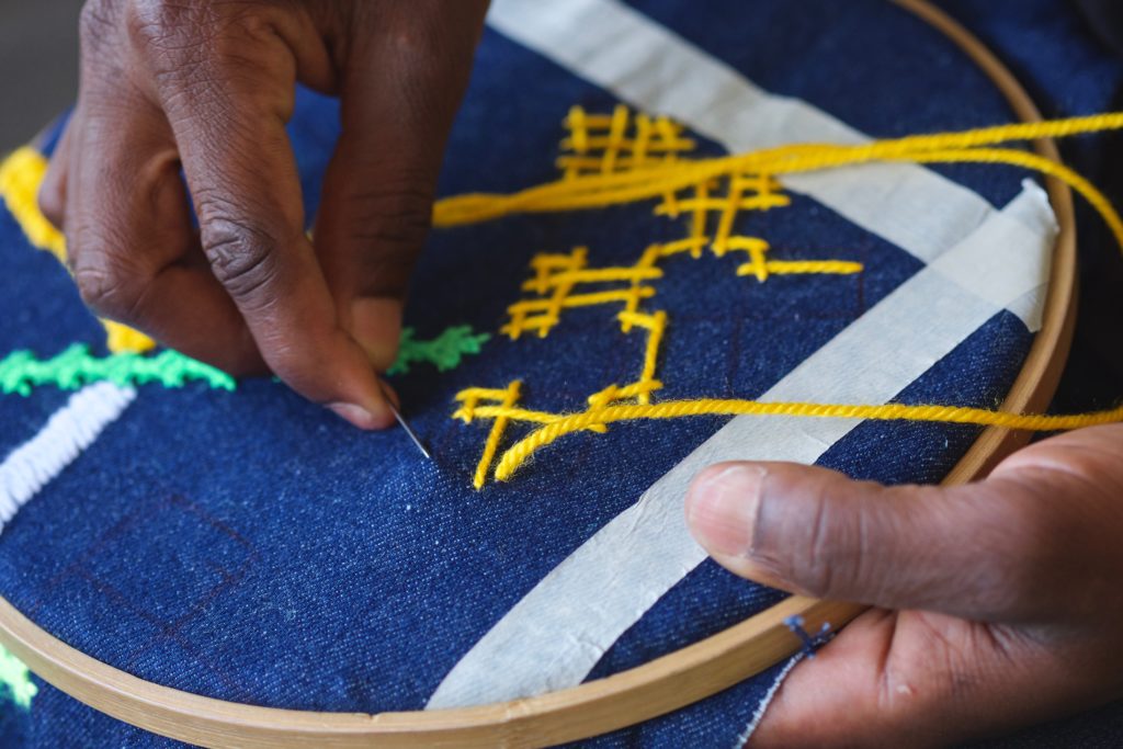 Hands sew a yellow pattern onto a blue fabric