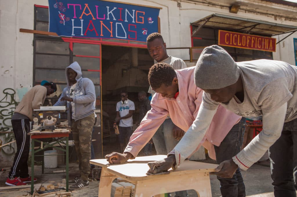 Two refugees do woodwork outside the Talking Hands Studio