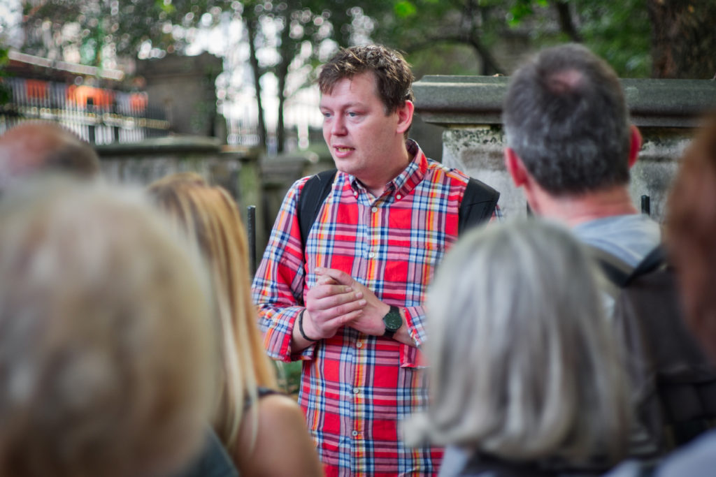 Guide wearing a red chequered shirt tells a story to tourists in a park